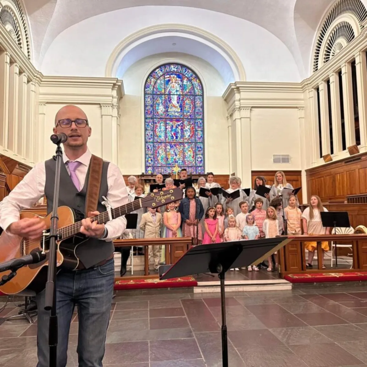 Matt Headley leading music on acoustic guitar with a children's choir behind him at Anniston First United Methodist Church